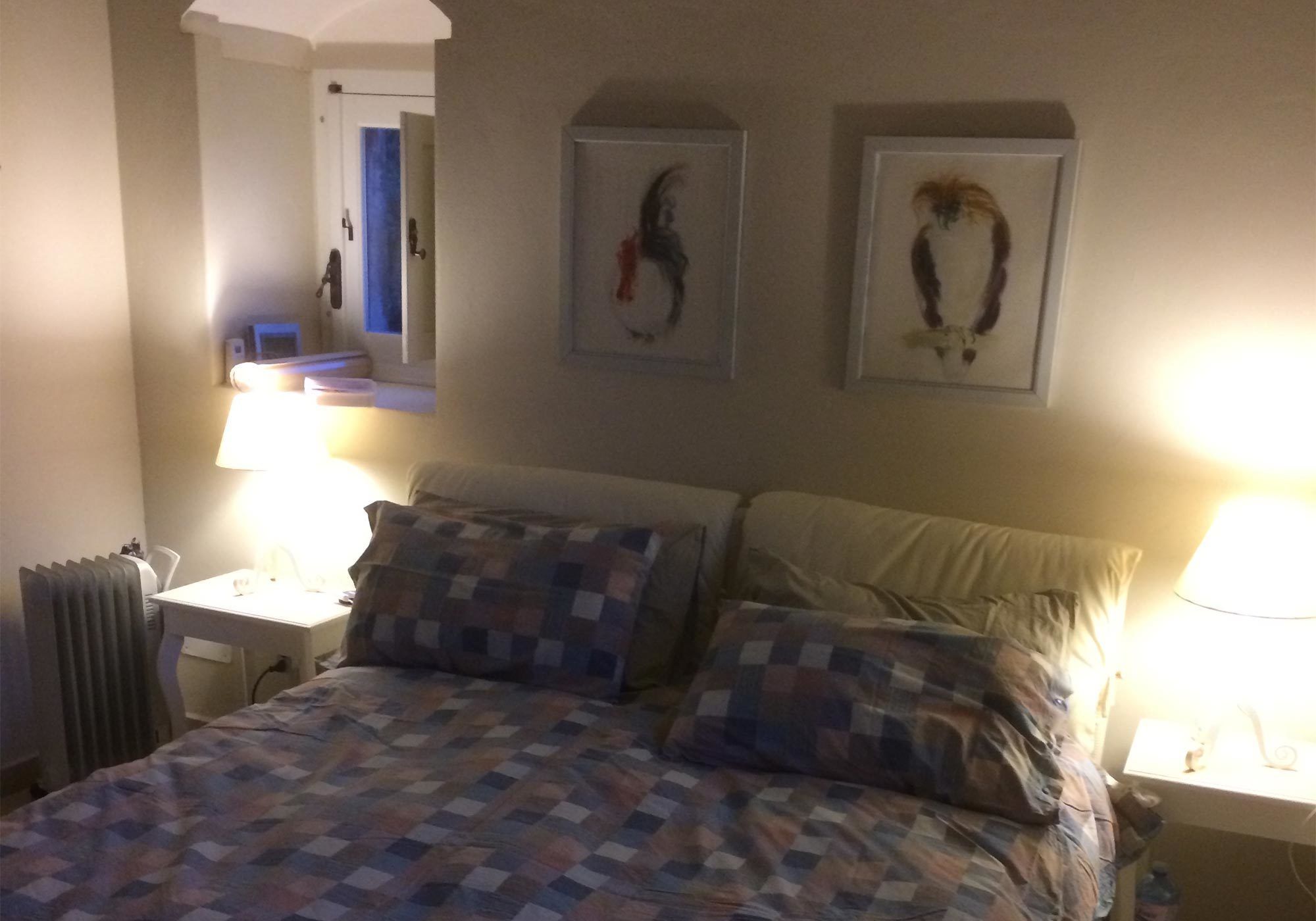 A hotel room with a bed, two bedside tables, a mirror, and two framed artworks on the wall.