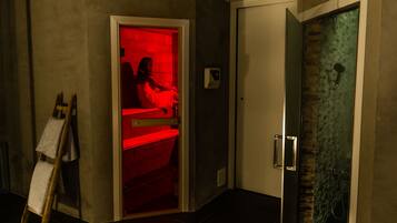 Ein Zimmer mit roter Beleuchtung in einer Ecke, eine Dusche mit Glastür und eine an der Wand lehnende Holzleiter.