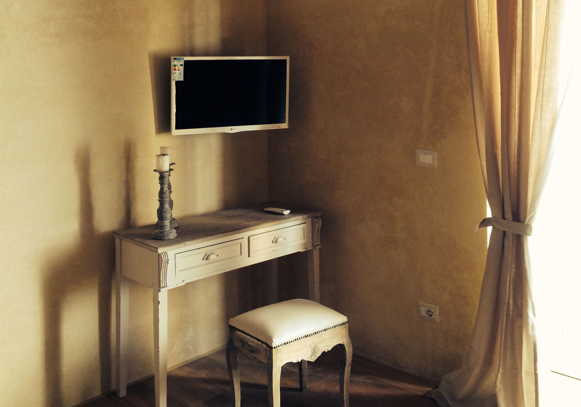 Een kamer met een bureau, een stoel, een aan de muur bevestigde televisie en een gordijn voor het raam.