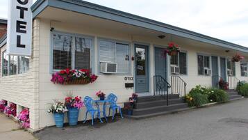 A motel with a front porch, blue chairs, and flower planters.