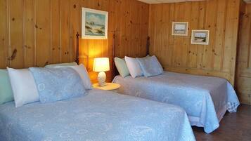 A room with two beds, wooden walls, and a painting on the wall.