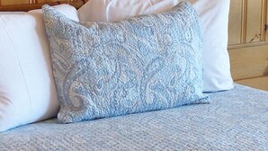Una cama con almohadas de diseño azul y blanco, un cabecero de madera y una lámpara sobre una mesita de noche de madera.