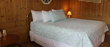 Une chambre à coucher comprenant un lit, une table de chevet, une lampe et un mur en bois orné d’un élément décoratif.
