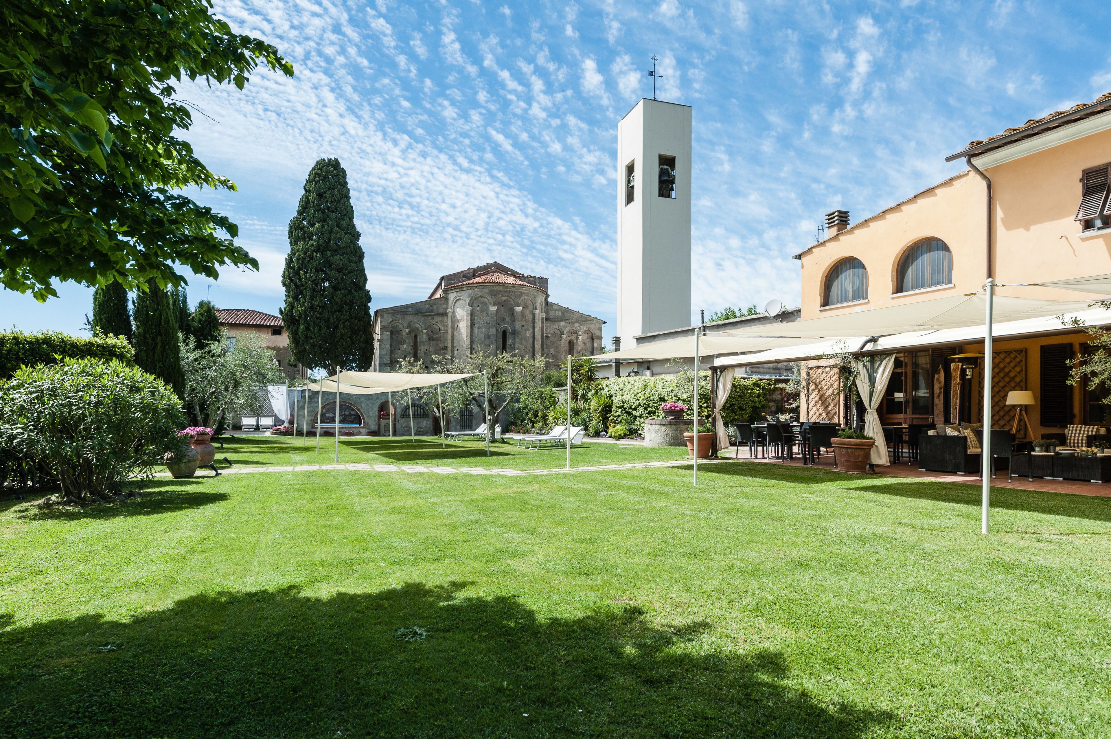 Un cortile con prato verde, un'alta torre bianca e un edificio con finestre ad arco.