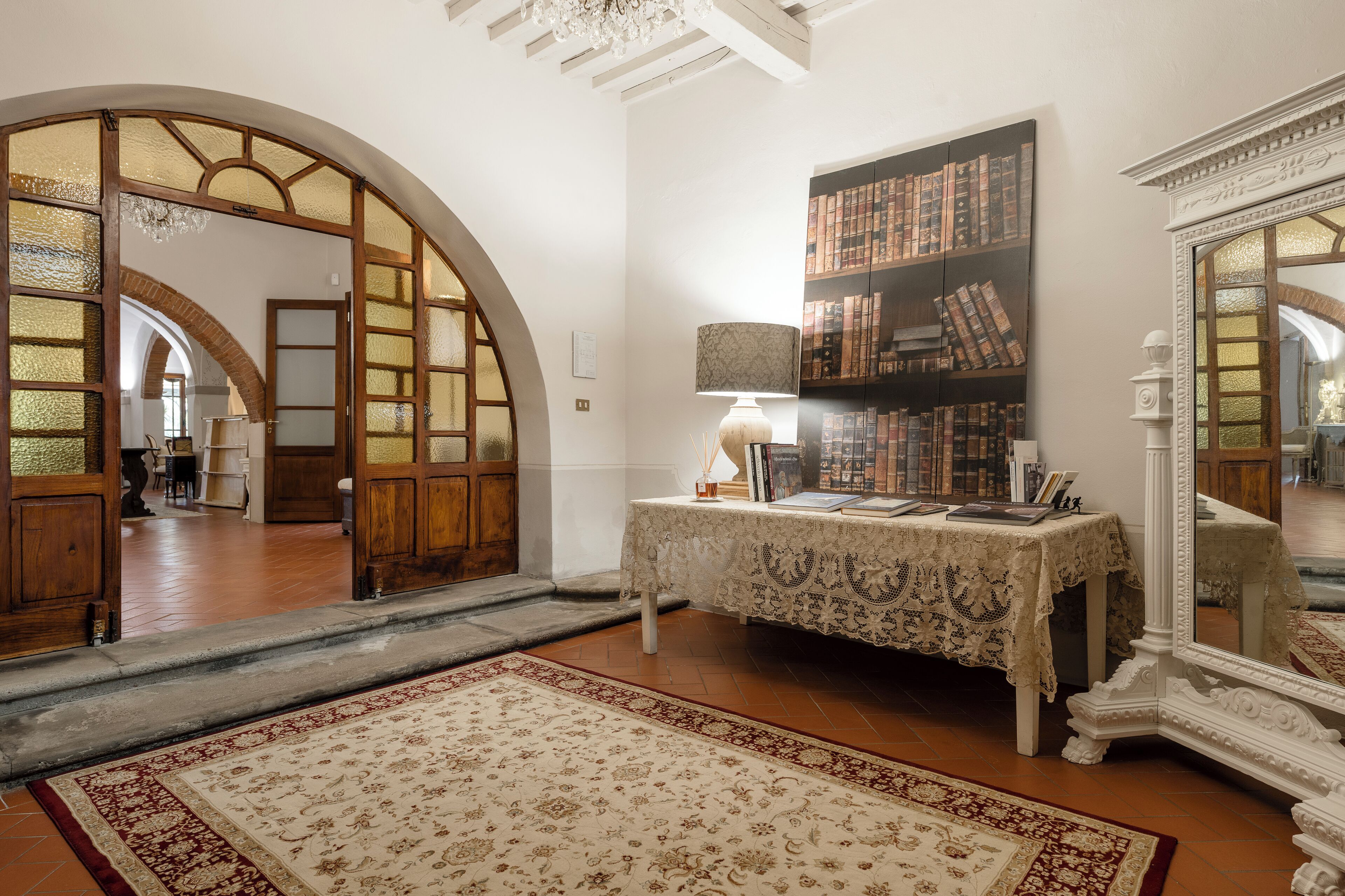 A room with a wooden door, a table with a lace tablecloth, a bookshelf, and a mirror.