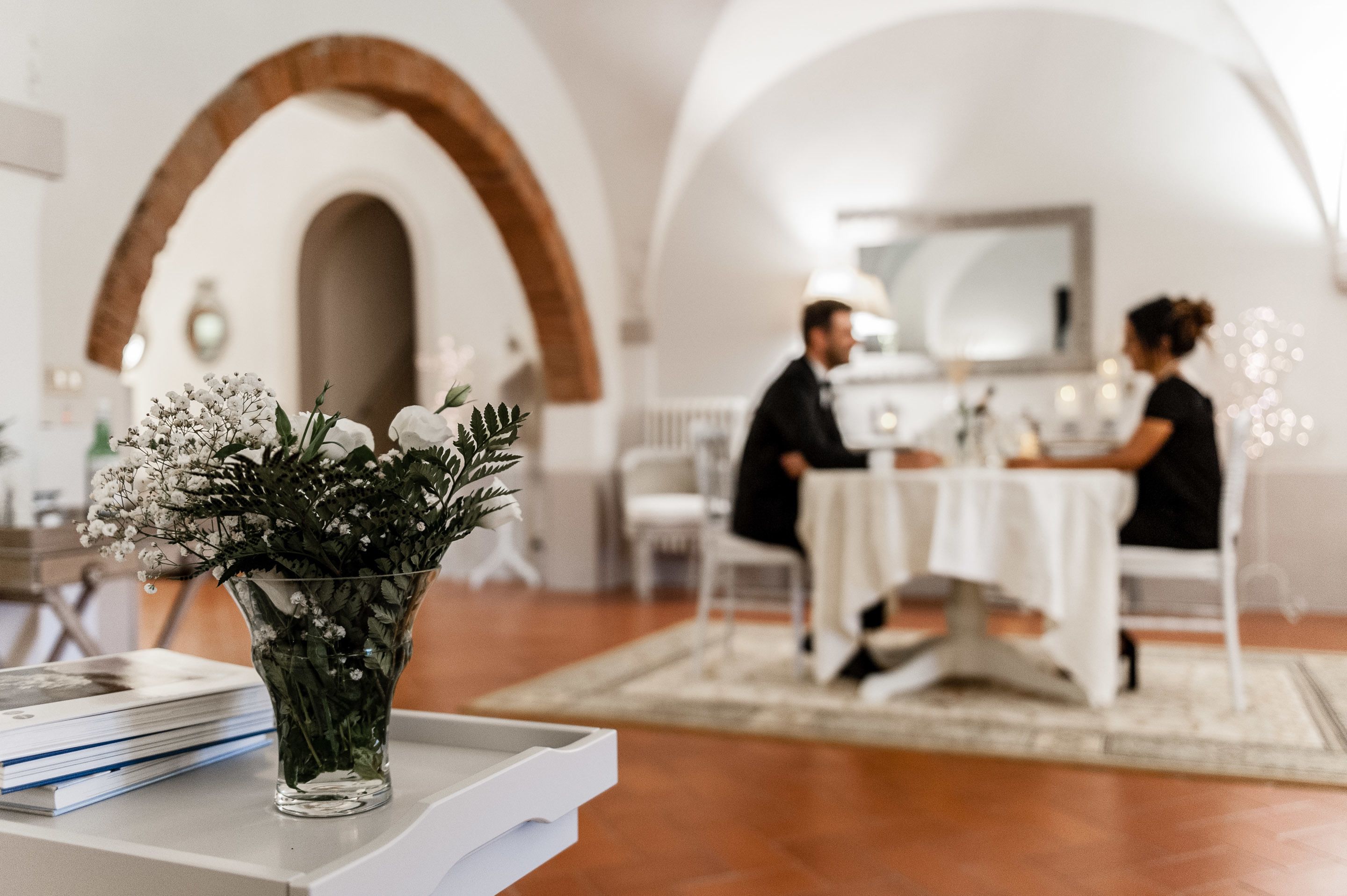 A dining area with a white table and chairs, a vase of flowers, and a brick archway.