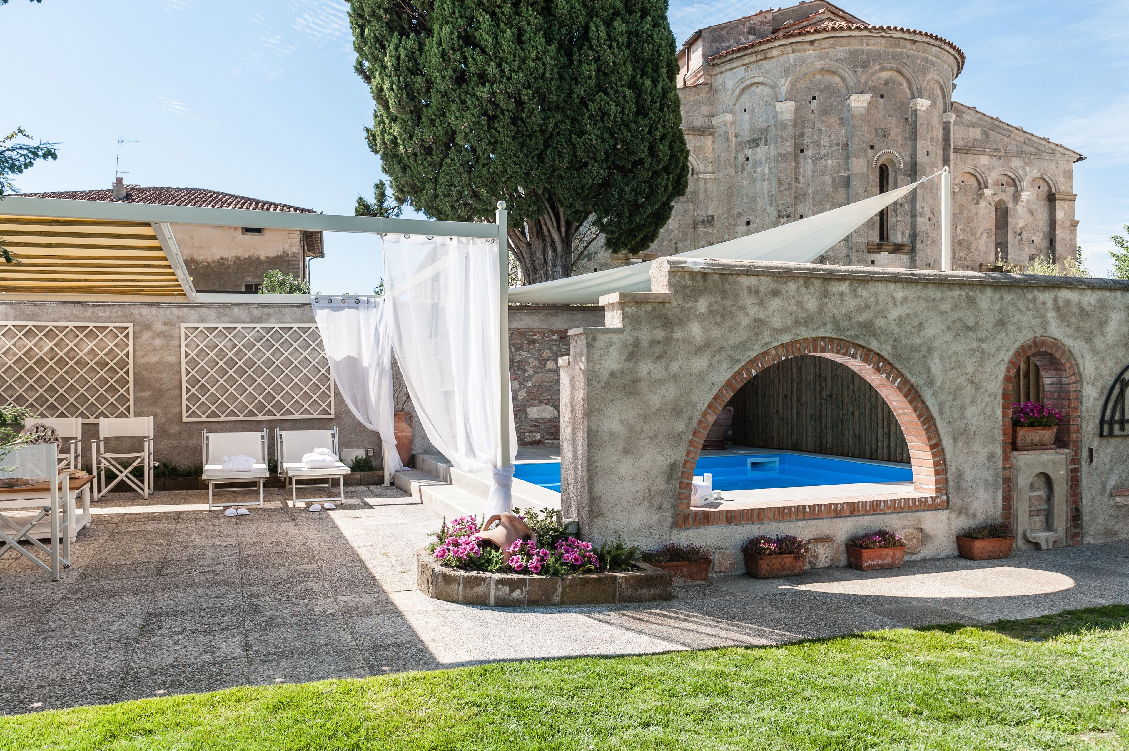 Un patio con piscina, mobiliario exterior y un edificio histórico al fondo.