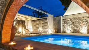 Un área de piscina al aire libre con un muro de piedra, una pérgola y sillones de descanso.