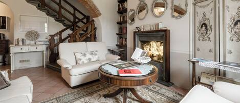 A living room with a white sofa, a round wooden coffee table, a fireplace, and a staircase.