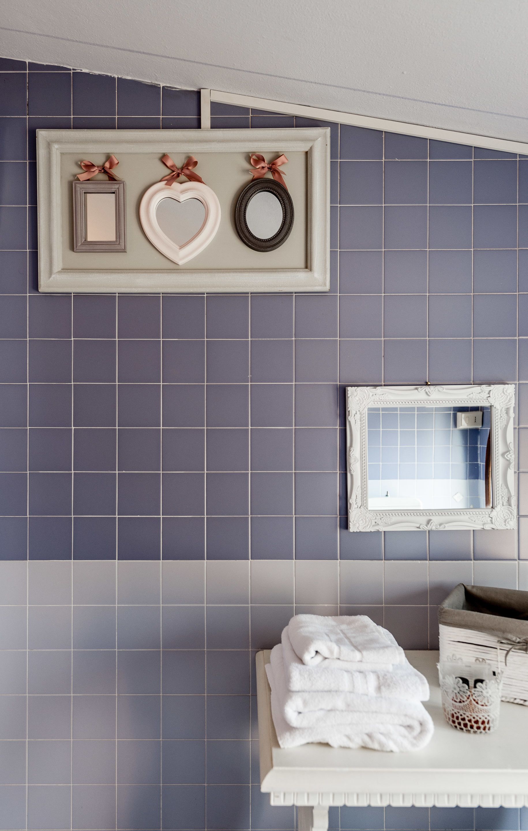 Een badkamer met een betegelde muur, een lijst met spiegel, een plank met handdoeken en decoratieve items.