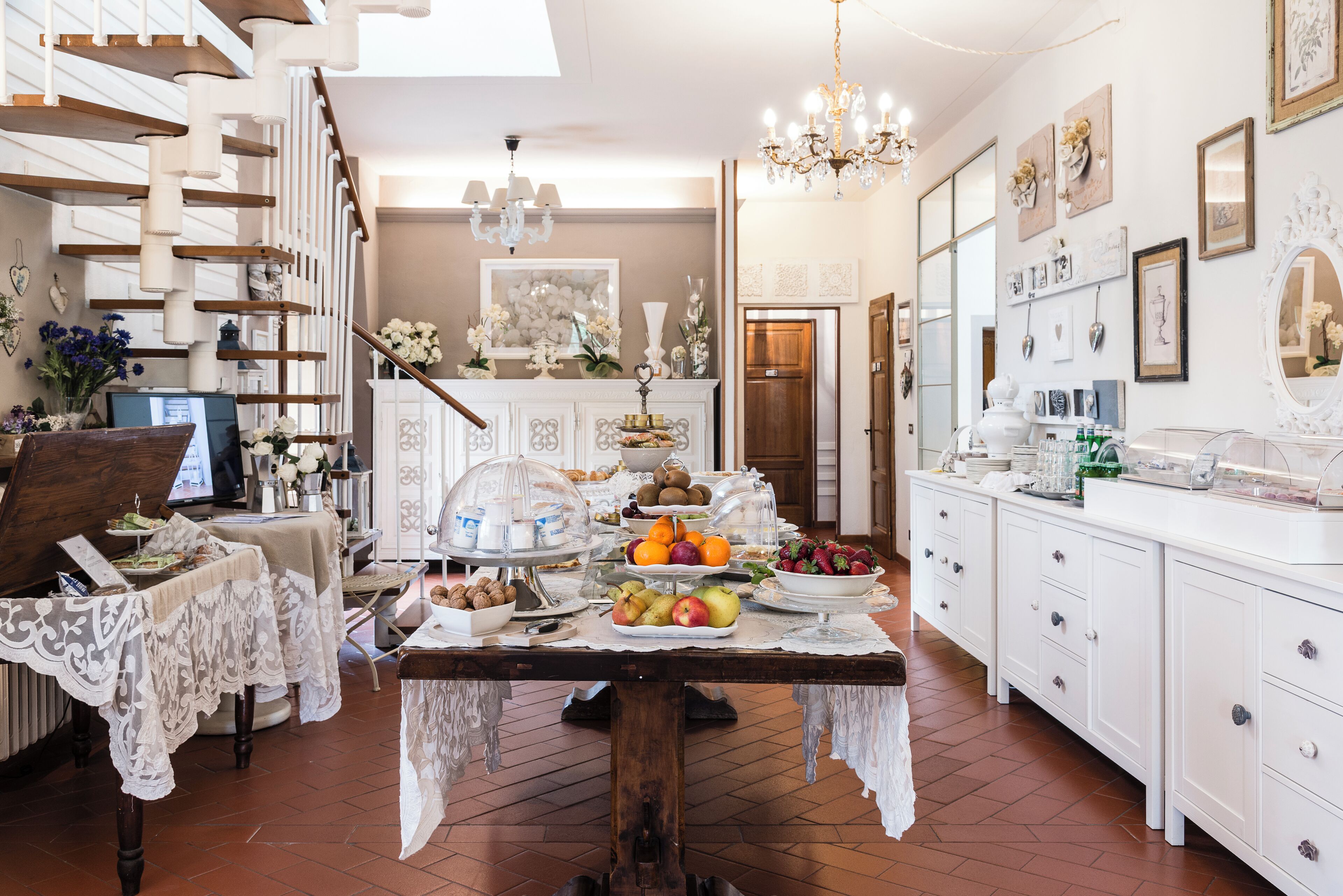 A well-lit kitchen with a dining table set for a meal, surrounded by white cabinetry and a staircase.