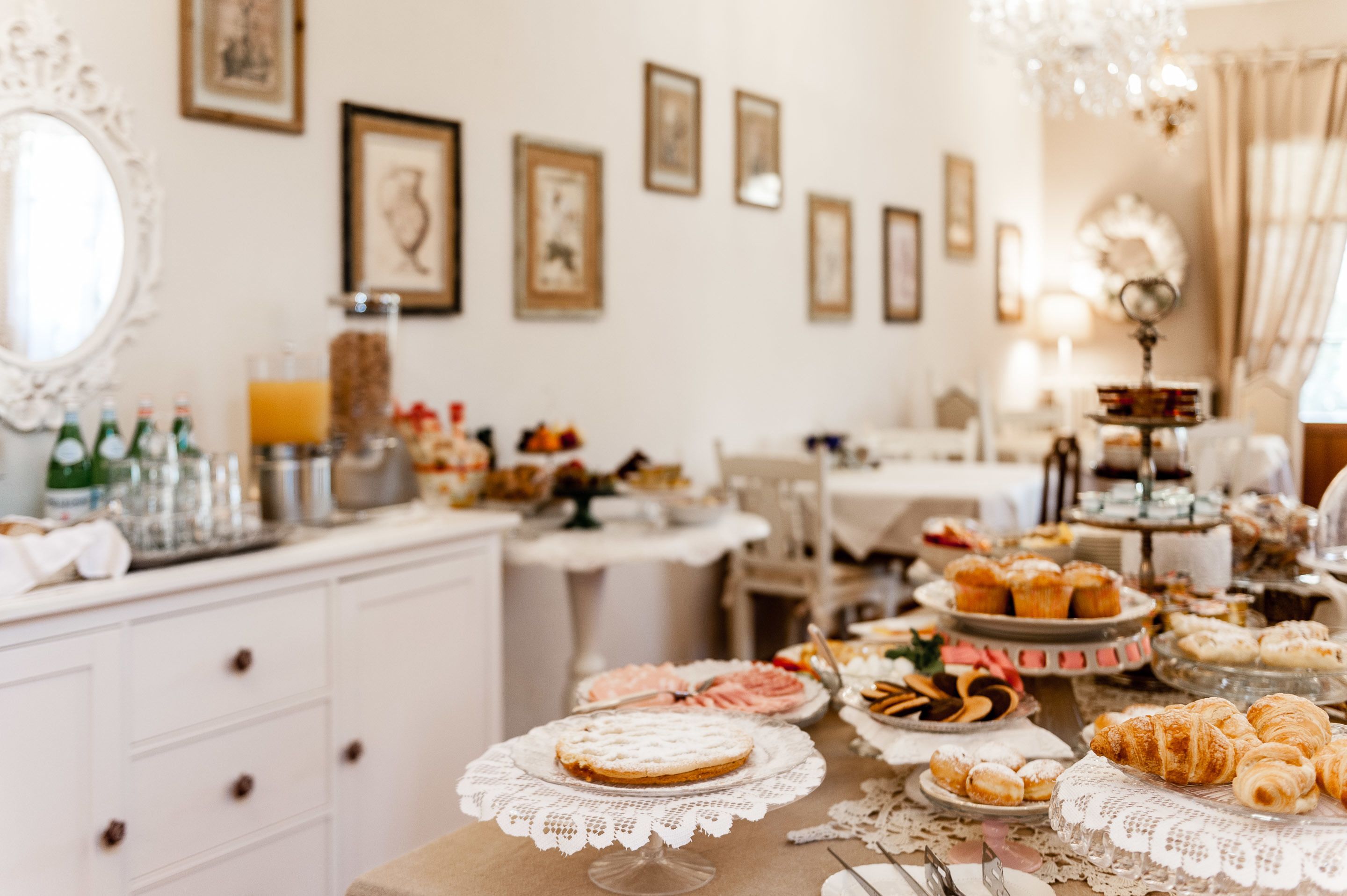 A buffet table with various pastries and desserts, a white cabinet with drawers, and framed artwork on the wall.