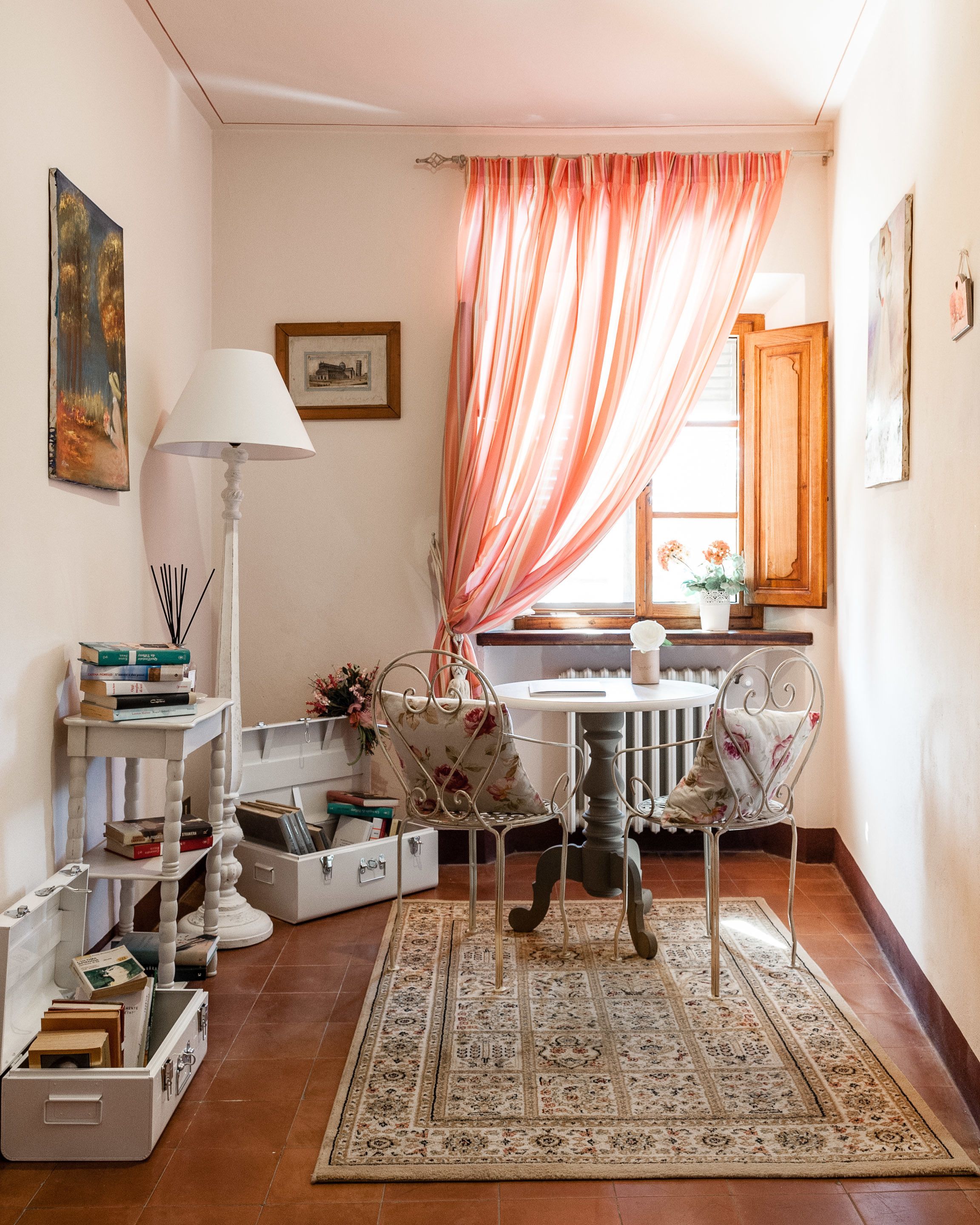 A cozy room with a dining table, chairs, a lamp, a bookshelf, and a window with curtains.