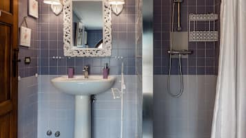 Une salle de bain avec un lavabo sur colonne, un grand miroir encadré de deux appliques murales, une douche avec un rideau et un carrelage à motifs à carreaux.