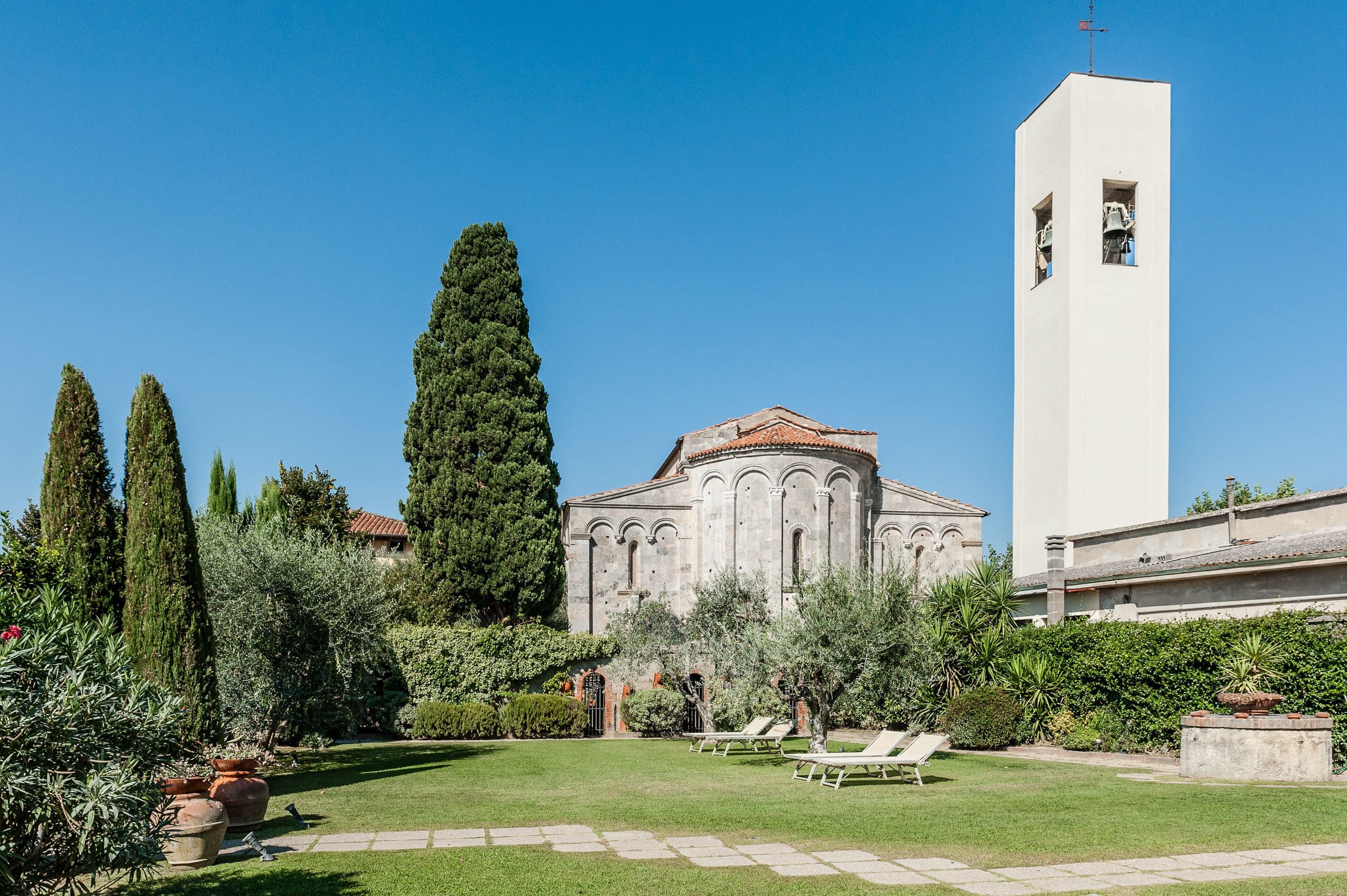 Un edificio histórico con un campanario, rodeado por un jardín bien cuidado con diversas plantas y un césped.