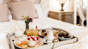 Bandeja de desayuno con diversas comidas y bebidas sobre una cama en una habitación de hotel.
