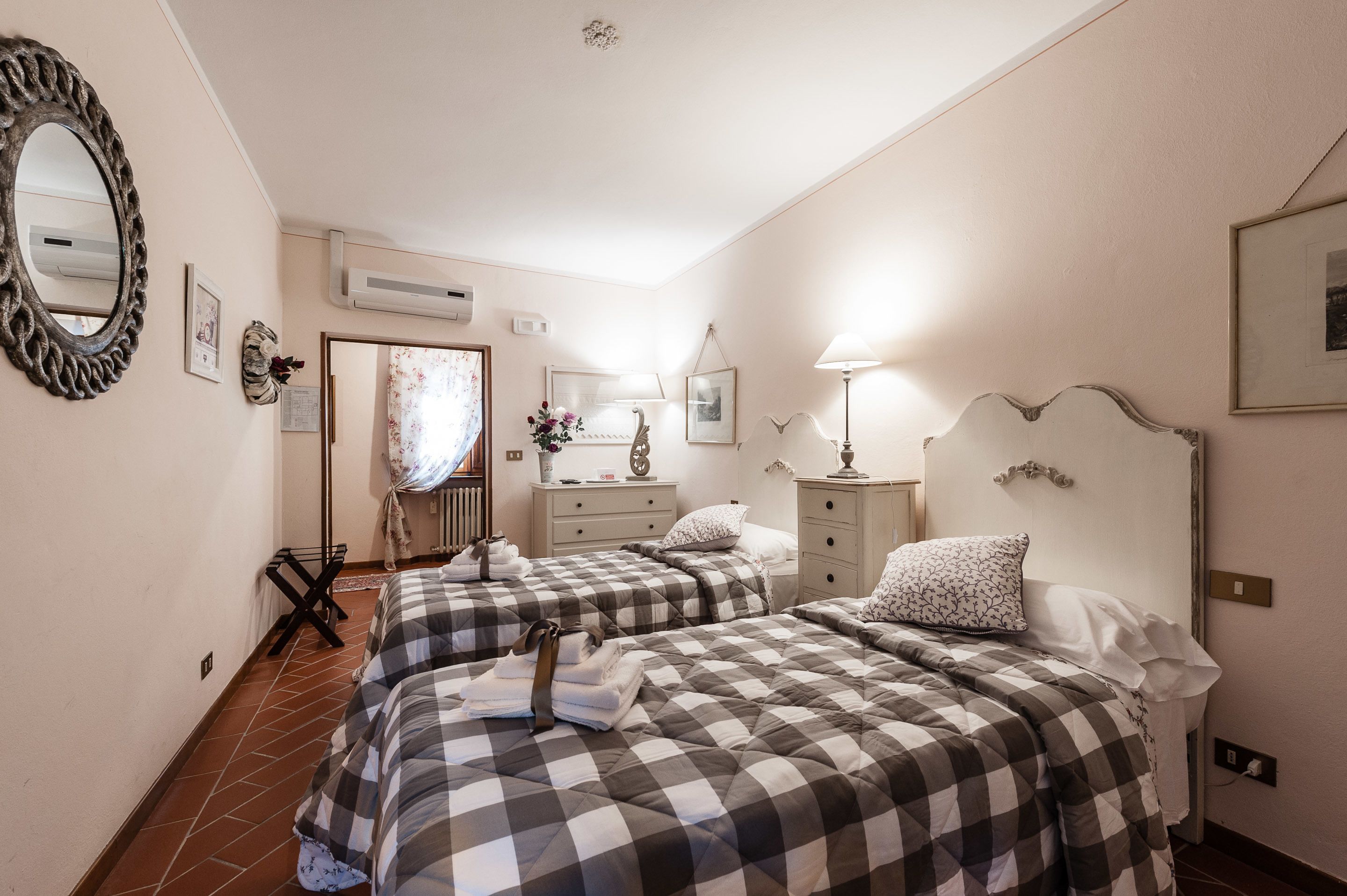 A hotel room with two beds, a large mirror, a dresser, and a window with curtains.