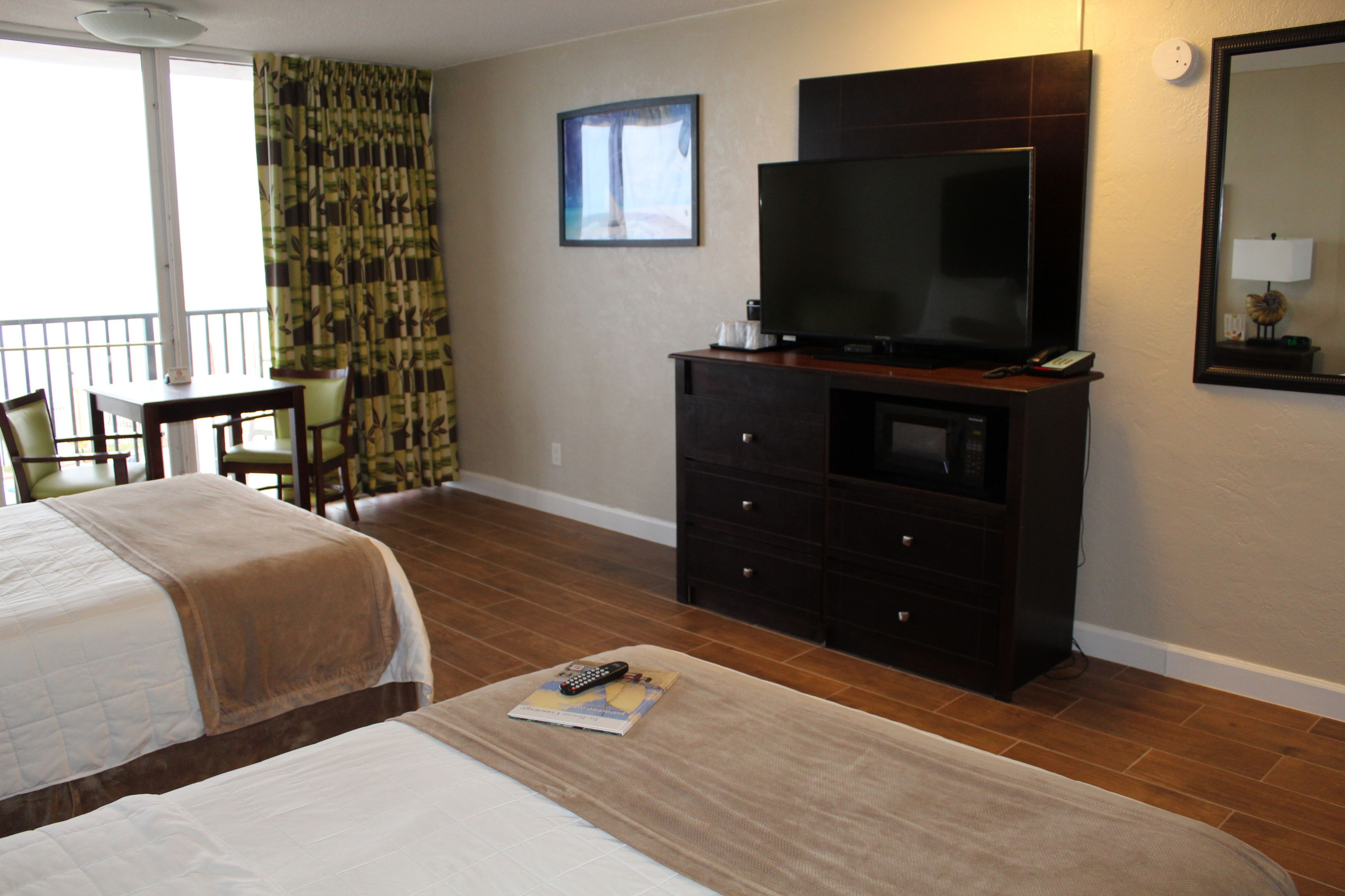 Habitación de hotel con dos camas, un televisor sobre un aparador, una silla y una ventana con cortinas.