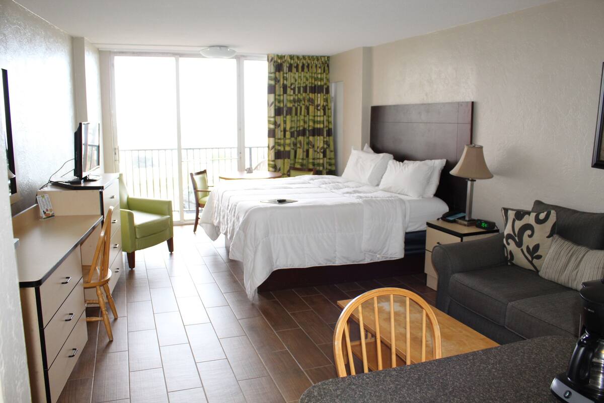 A hotel room with a bed, a desk, a chair, a sofa, and a coffee maker.