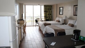 A hotel room with a kitchenette, two beds, a dining table, and a balcony with curtains. - Cove Motel Oceanfront (Daytona Beach)