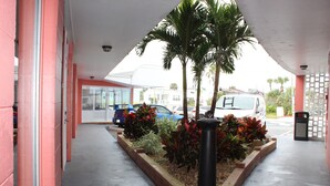 A parking area with a covered section, a planter with tropical plants, and a security camera. - Cove Motel Oceanfront (Daytona Beach)