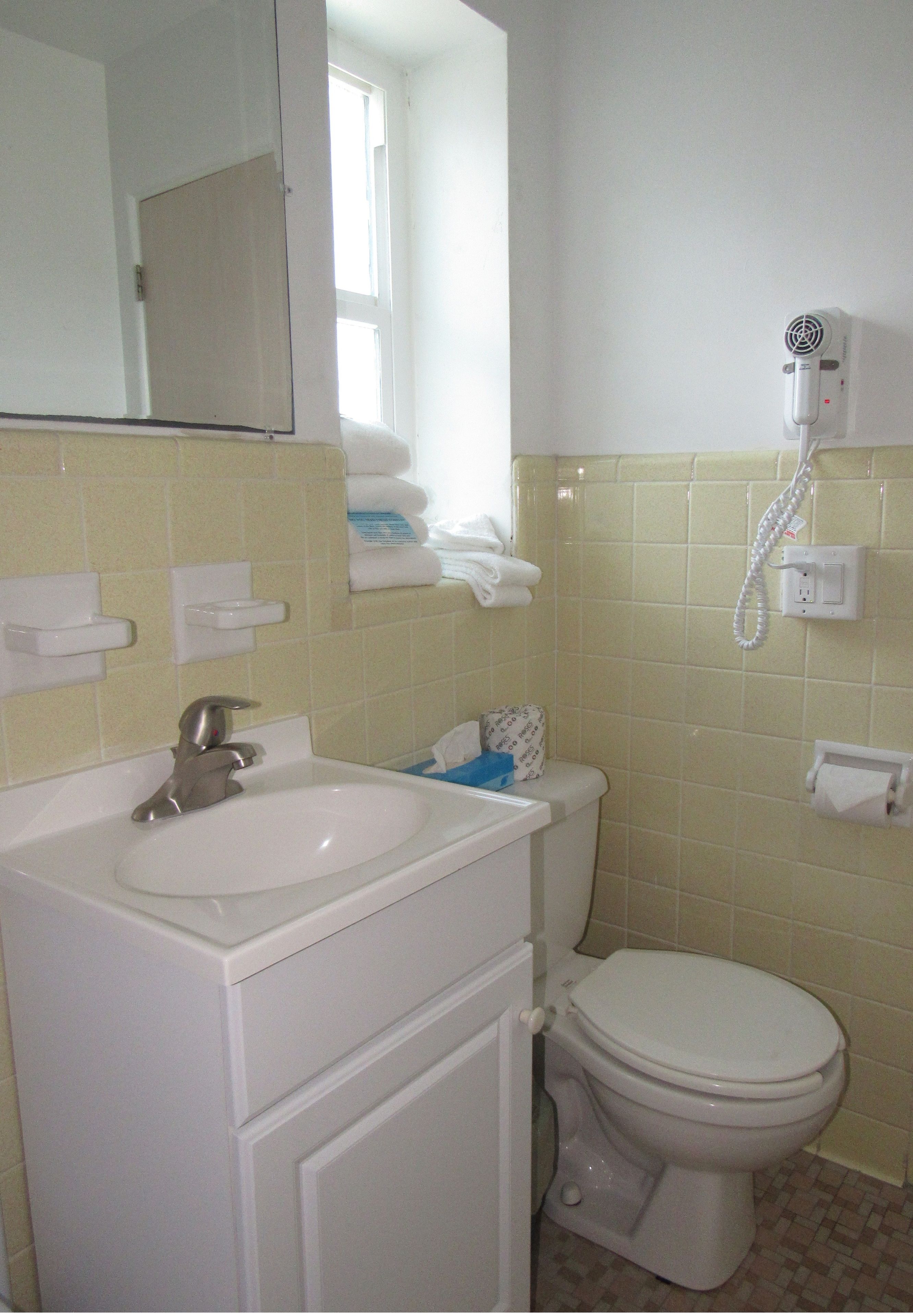 A bathroom with a sink, mirror, toilet, and a hairdryer mounted on the wall.
