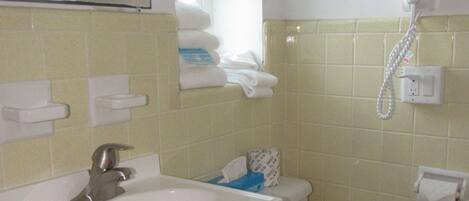 A bathroom with a sink, mirror, toilet, and a hairdryer mounted on the wall.