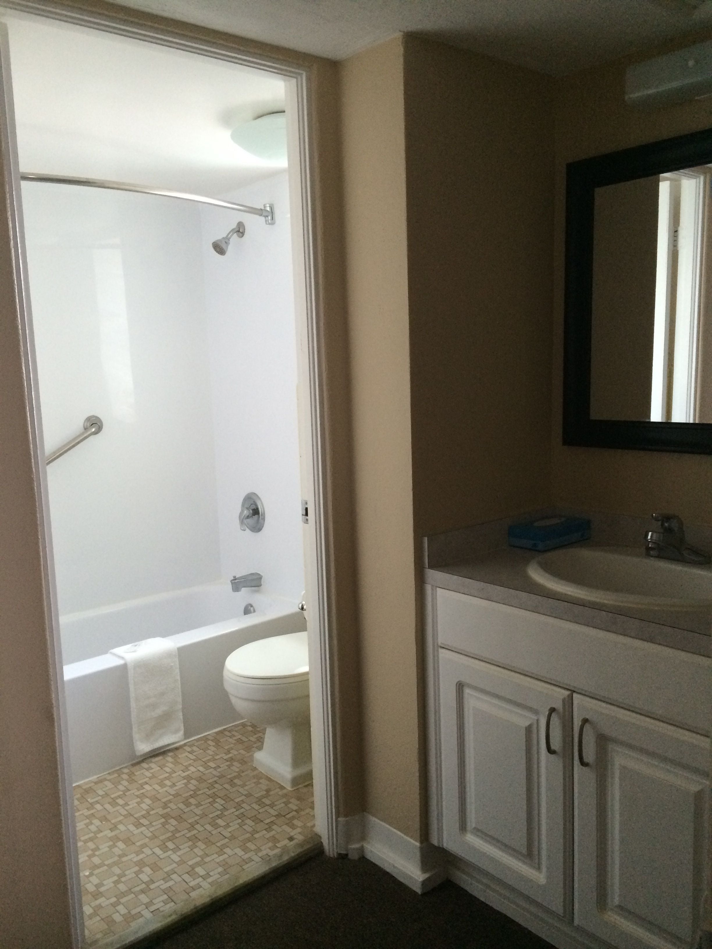 A bathroom with a shower, toilet, sink, and mirror.