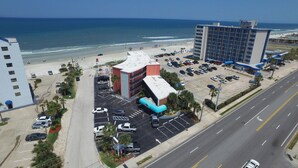 An aerial view of a hotel with a parking lot, a swimming pool, and a beach in the background. - Cove Motel Oceanfront (Daytona Beach)