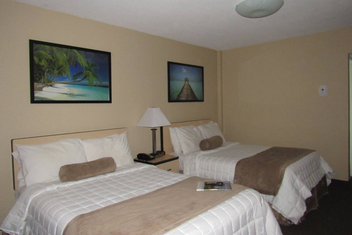 A hotel room with two beds, a nightstand with a lamp, and two framed pictures on the wall.