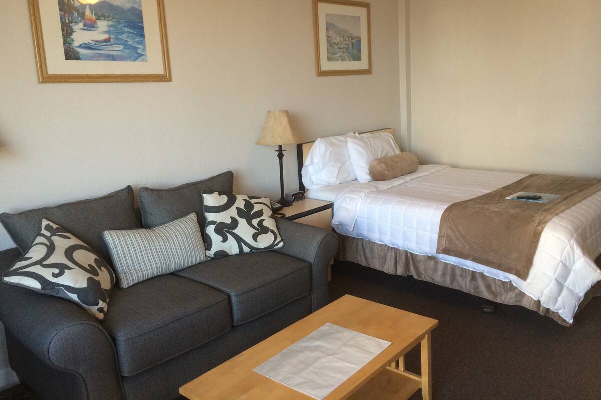 A room with a sofa, a bed, a nightstand, and two framed pictures on the wall.