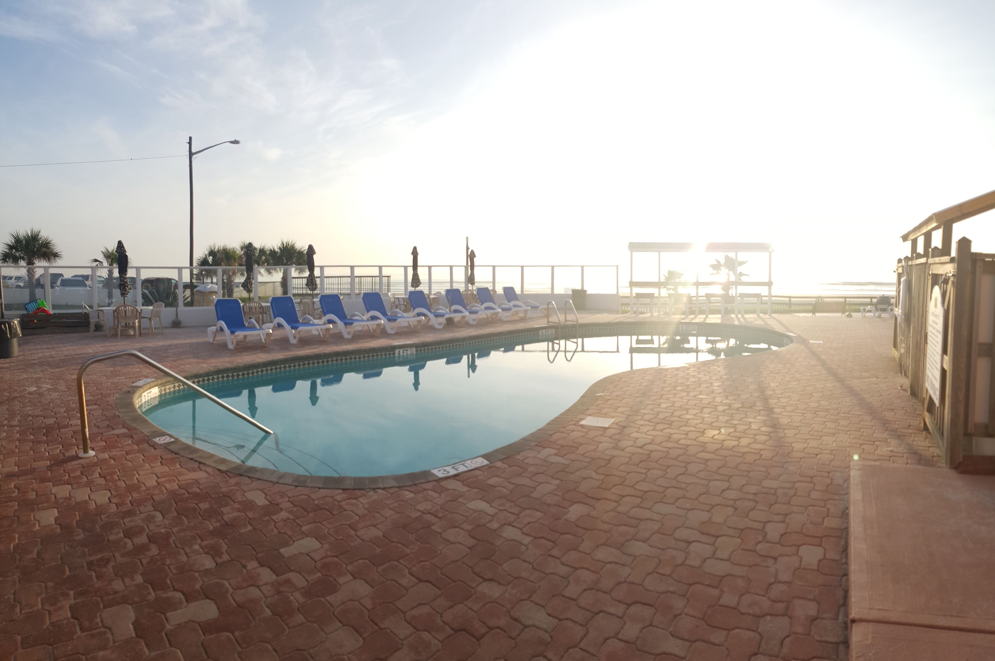 A pool area with blue lounge chairs and a brick pathway.