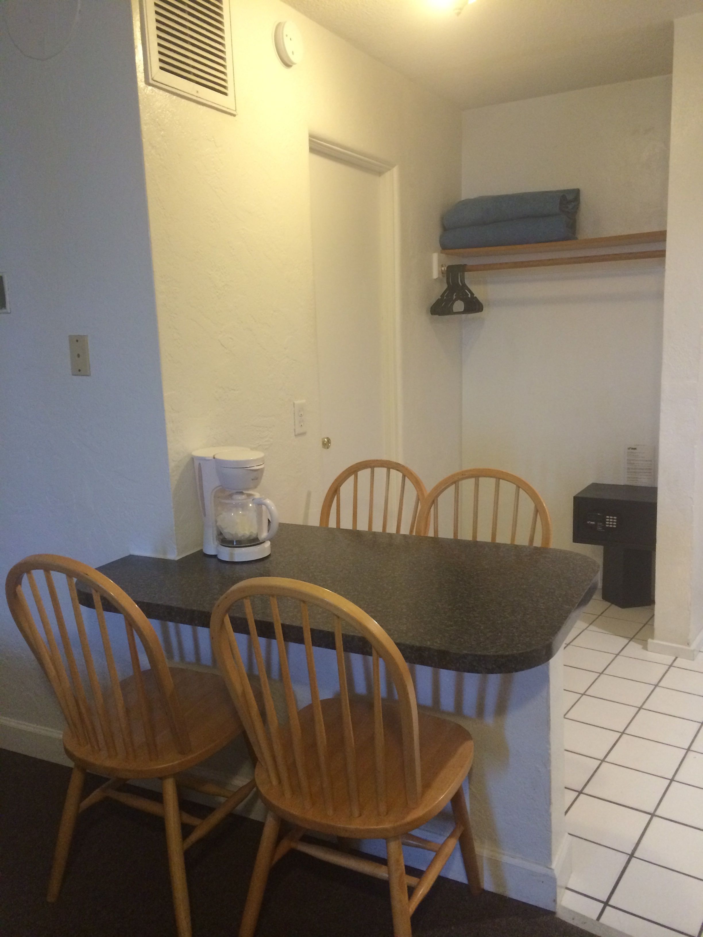 Una cocina pequeña con una mesa de comedor, dos sillas de madera, una cafetera y un electrodoméstico negro sobre la encimera.