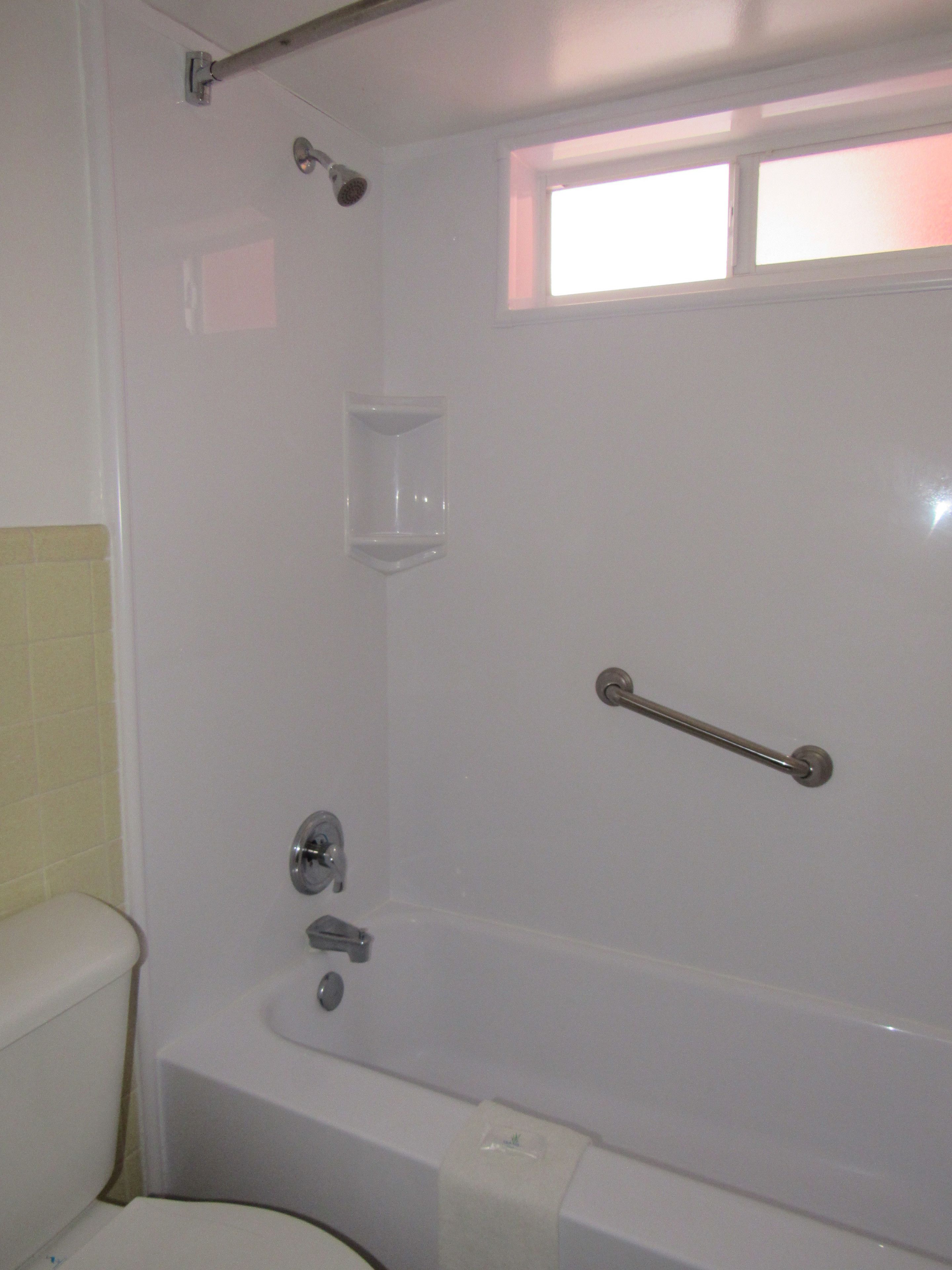 A bathroom with a bathtub, toilet, and a window.