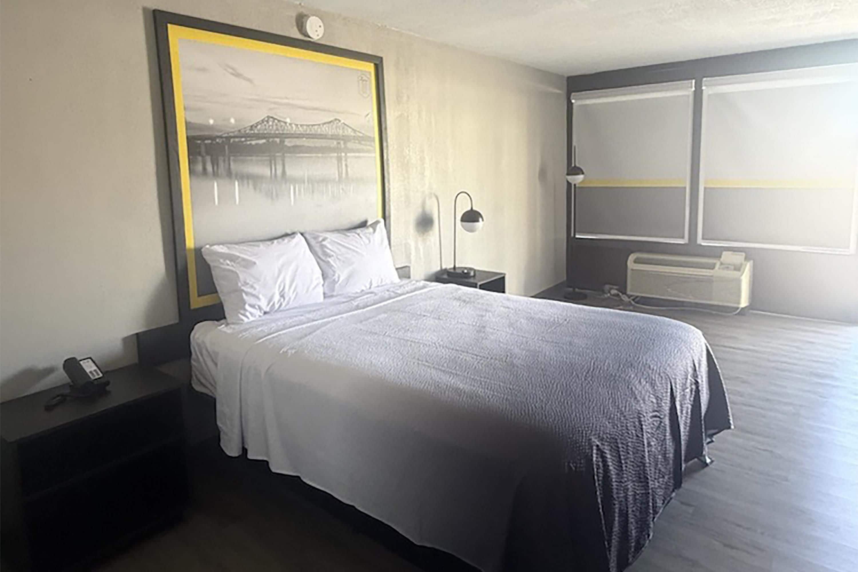 Habitació d'hotel amb llit, taula de nit, làmpada i una finestra gran.