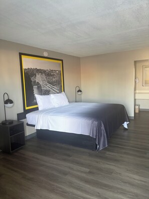 A bedroom with a bed, a nightstand, a lamp, a framed picture on the wall, and a door. - Tourway Inn (Birmingham)