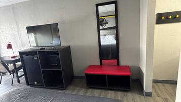 Una habitación de hotel con una cama, un escritorio con una computadora, un espejo y un banco rojo.