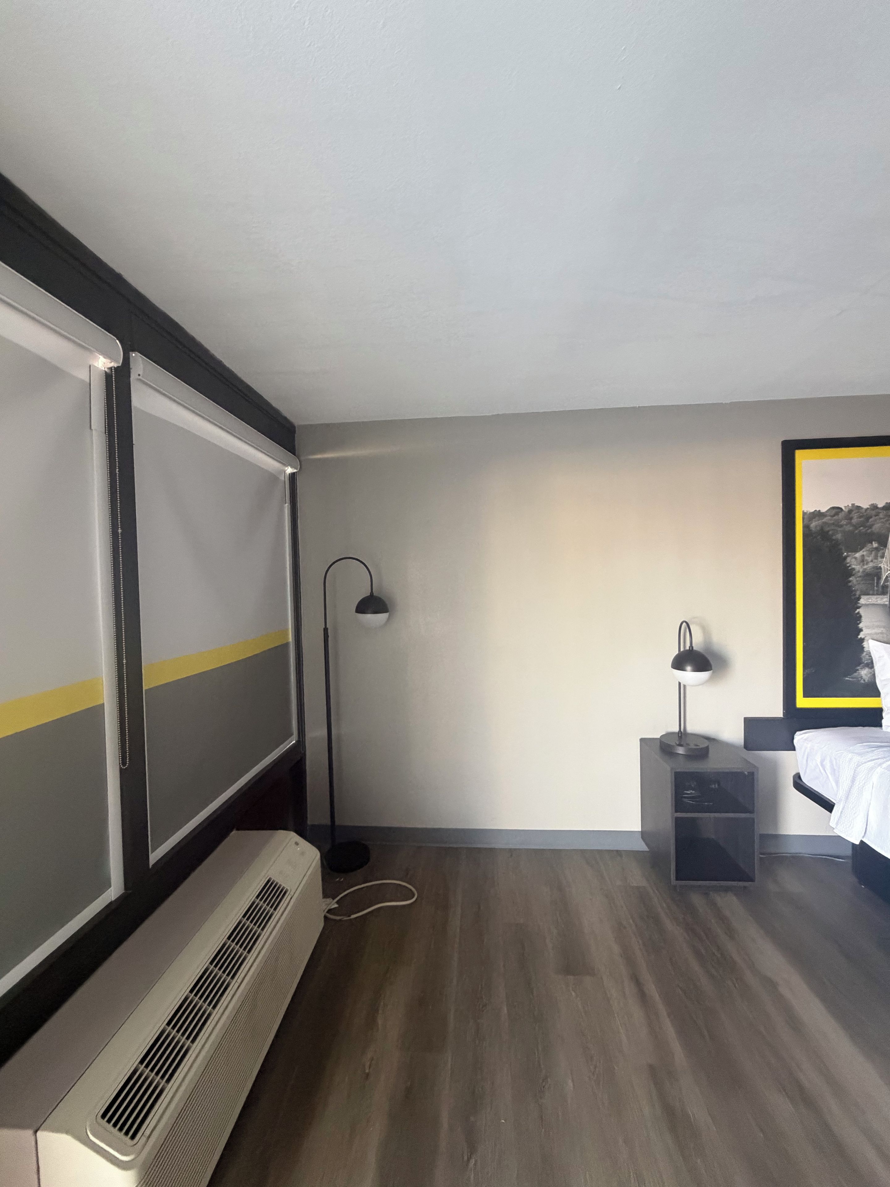 Een hotelkamer met een bed, een bureau, een staande lamp en een groot raam.