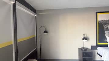 Een hotelkamer met een bed, een bureau, een staande lamp en een groot raam.