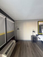 Una habitación de hotel con cama, escritorio, lámpara de pie y un ventanal grande.