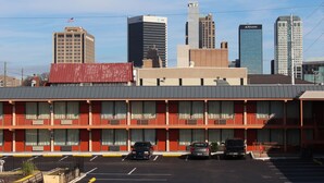 Un motel con estacionamiento, una estructura de dos pisos y un horizonte urbano al fondo.