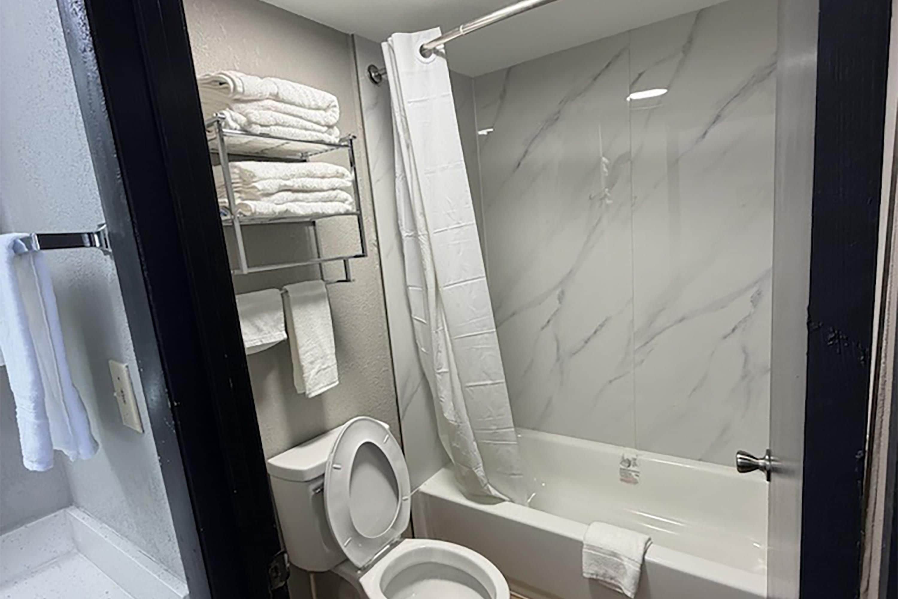 A bathroom with a toilet, a shower, and a bathtub. There are towels on a rack.