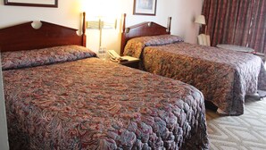Habitación de hotel con dos camas dobles, una mesita de noche con lámpara, una silla y una cortina.