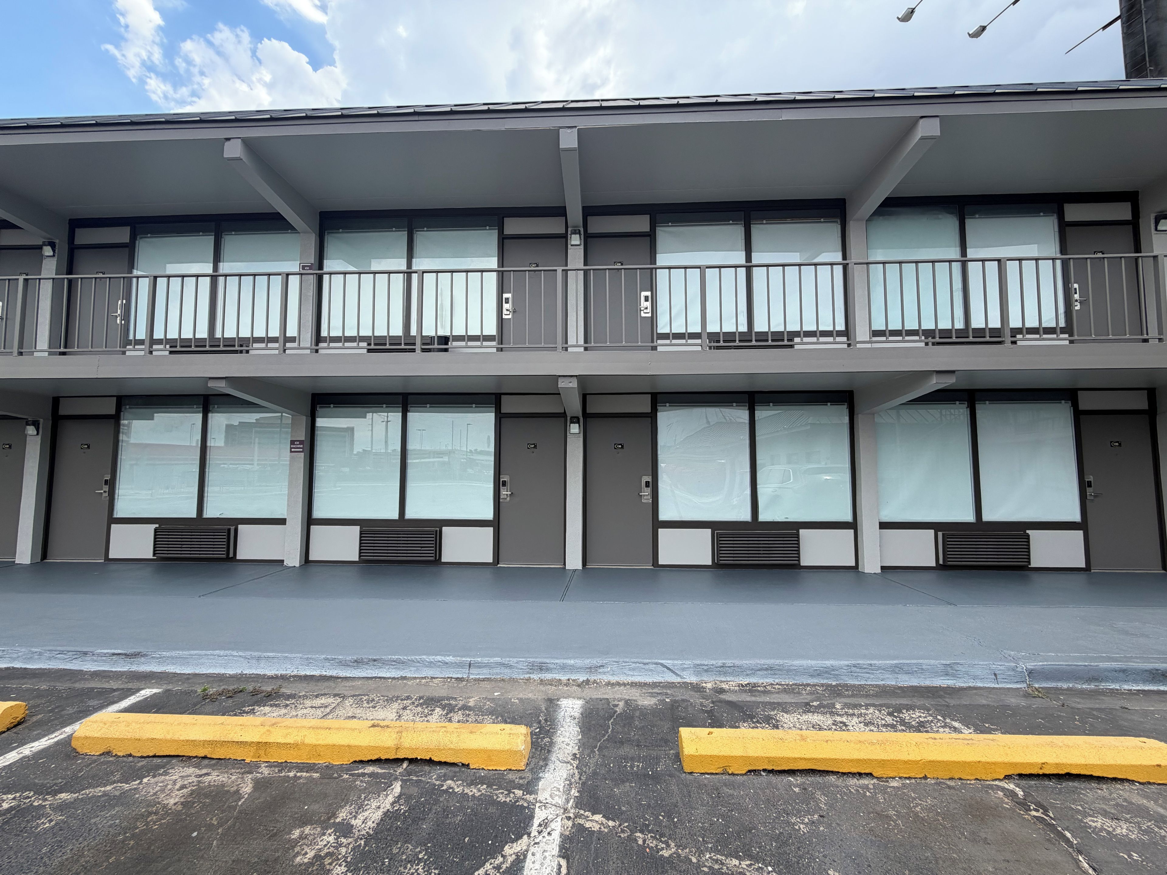 A multi-story building with large windows, a balcony on the upper floor, and a parking area with yellow curbs.