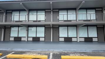 Un edificio de varios pisos con amplios ventanales, un balcón en el nivel superior y un estacionamiento con bordillos amarillos.