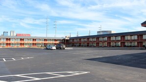 Un estacionamiento con espacios delimitados, un edificio rojo con varias ventanas y algunos automóviles estacionados.