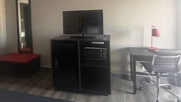 Habitación de hotel con una cama, un escritorio con una silla, un televisor sobre un mueble y una lámpara roja.