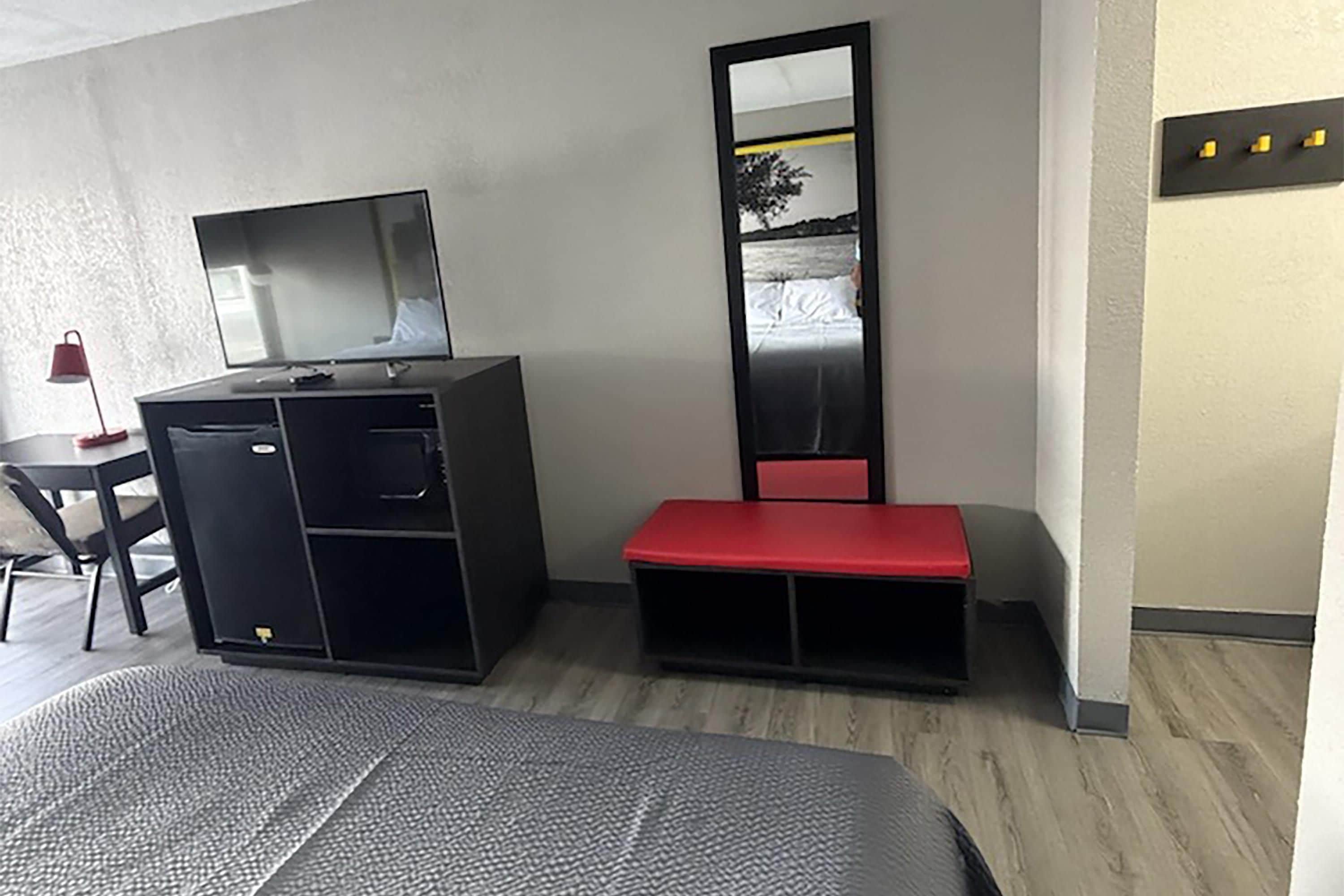 Habitació d'hotel amb un llit, un escriptori amb una cadira, un armari, una panxa de daina i un mirall gran.