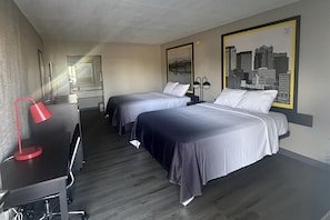 A hotel room with two beds, a desk, a chair, a red lamp, and a cityscape painting on the wall. - Super 8 by Wyndham Birmingham Downtown (Birmingham)