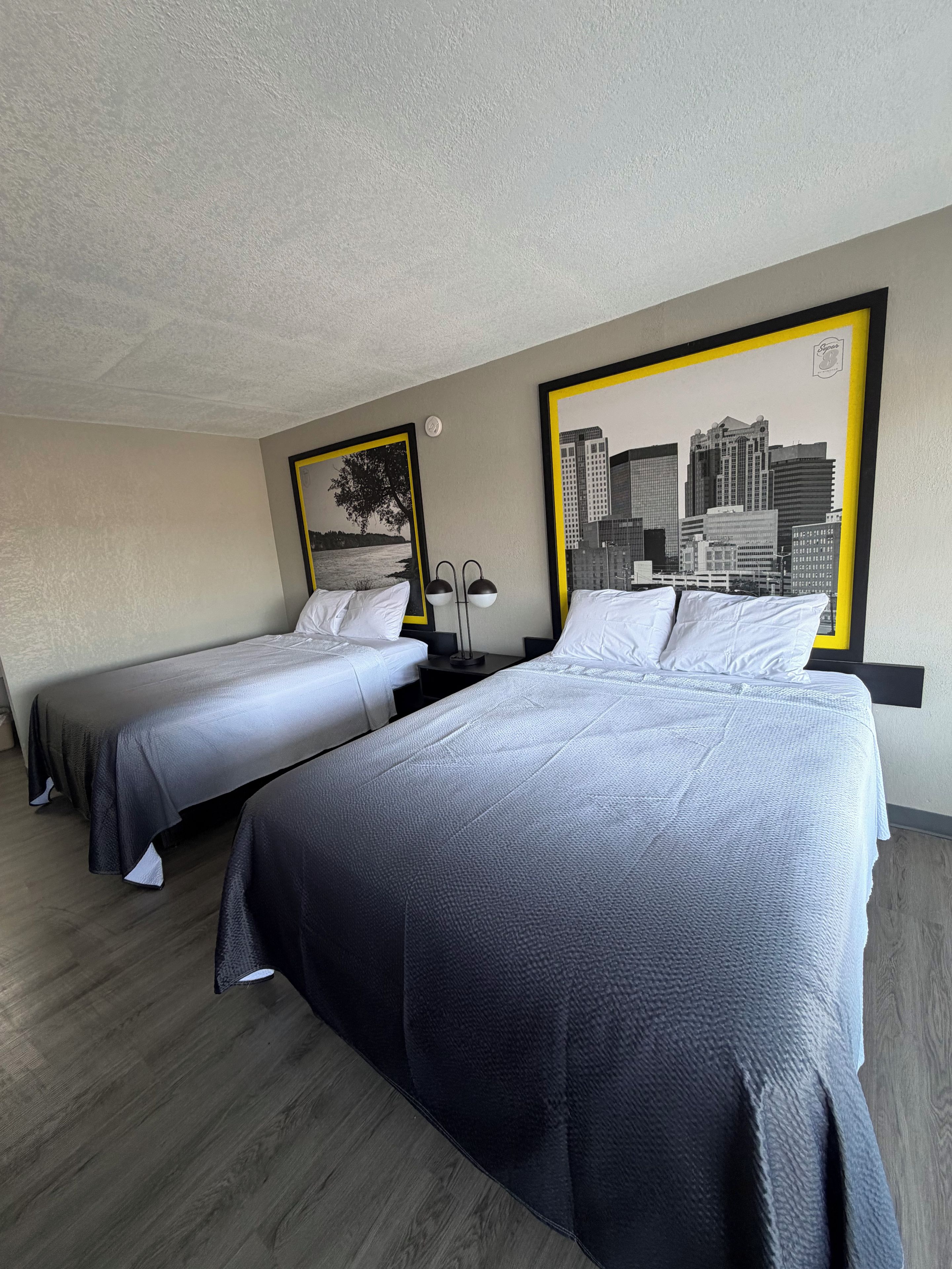 Habitación de hotel con dos camas, un cuadro de un paisaje urbano y una lámpara.